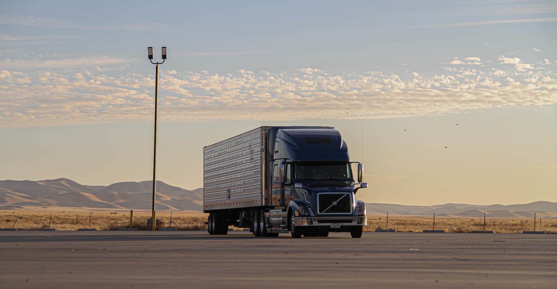 Blue Volvo semi truck on the highway at golden hour — insured by NITIC